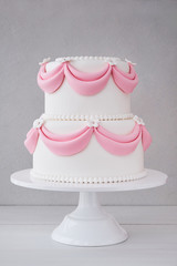 White wedding cake with pink elements made from pastry mastic on a wooden background. Sugar flowers, marzipan flowers and mastic, beautiful decor for decorating cakes.