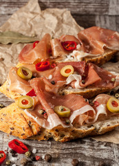 Fototapeta na wymiar Bruschetta with roasted bell pepper, prosciutto, garlic, olives, spices and herbs. Appetizers.
