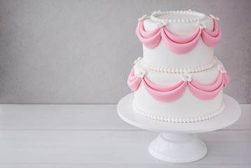 White wedding cake with pink elements made from pastry mastic on a wooden background. Sugar flowers, marzipan flowers and mastic, beautiful decor for decorating cakes.