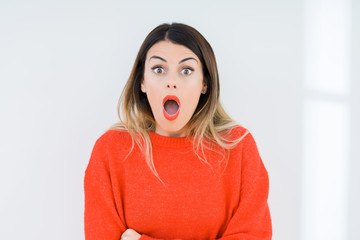 Young woman wearing casual red sweater over isolated background afraid and shocked with surprise expression, fear and excited face.