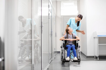 Young female doctor taking care of little girl in wheelchair indoors