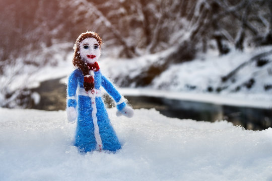 Handmade doll needle felted from a wool stands in the snow on the shore of the winter river