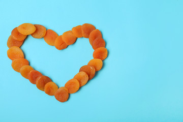 Heart shaped frame made of dried apricots on color background, top view with space for text. Healthy fruit
