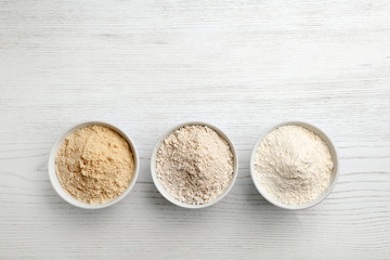 Bowls with different types of flour on white wooden background, top view. Space for text