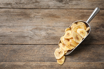 Scoop with banana slices on wooden background, space for text. Dried fruit as healthy snack