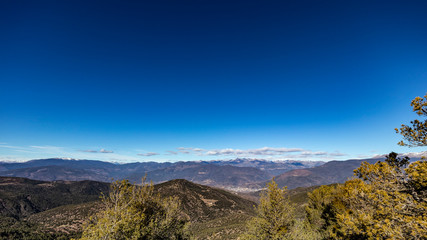 Fototapeta premium Solid blue sky on a mountain range landscape with some clouds on a green winter scene