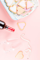 Happy Valentine's day greeting card with heart cookies, wine glasses and wine on pastel pink background.