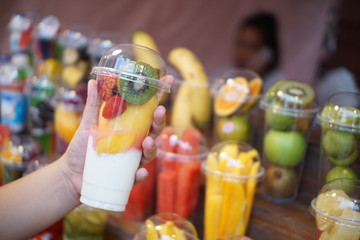 Banglamung ,Chonburi/Thailand-June 23,2018 : Close-up women hand holding Mix Fruits in a plastic Glass with Wooden shelves at Street food market,Thailand.