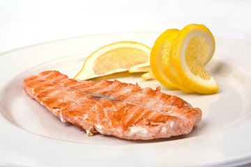 Grilled salmon with lemon on a white plate, close-up