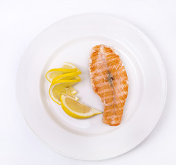Salmon on grill with lemon on a white plate, top view
