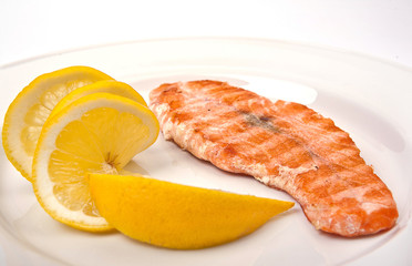 Salmon on grill with lemon on a white plate, macro