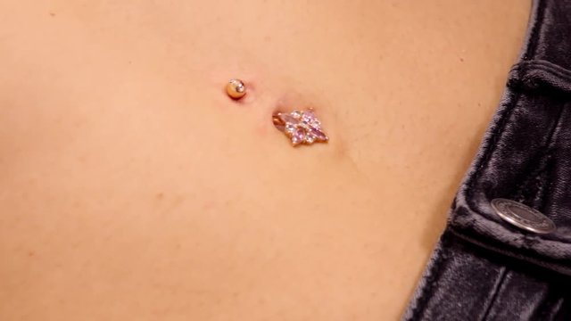 slow motion closeup piercing master in gloves wipes skin with cotton napkin around gold sparkling belly button ring 