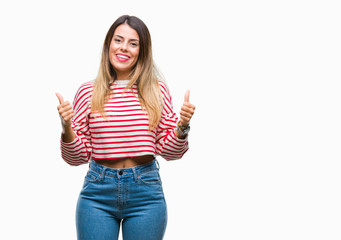 Obraz premium Young beautiful woman casual stripes winter sweater over isolated background success sign doing positive gesture with hand, thumbs up smiling and happy. Looking at the camera with cheerful expression
