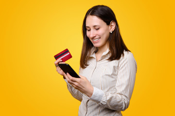 Cheerful young woman in casual using smartphone and holding credit card