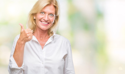 Fototapeta premium Middle age blonde business woman over isolated background doing happy thumbs up gesture with hand. Approving expression looking at the camera with showing success.