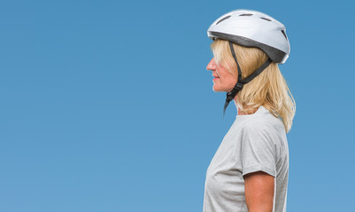 Middle age caucasian cyclist woman wearing safety helmet over isolated background looking to side, relax profile pose with natural face with confident smile.