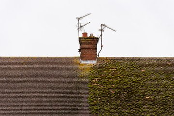 cloudy day view traditional british house roof with chimney half full with moss and half cleaned © Jevanto Protography