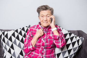 Theme old person uses technology. Mature happy joy smile active gray hair Caucasian wrinkles woman sitting home in living room on the sofa and using a mobile phone, calling and talking on the phone