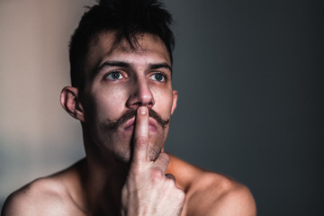 Young shirtless man with mustache thinking by the window