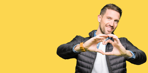 Handsome man wearing winter coat smiling in love showing heart symbol and shape with hands. Romantic concept.