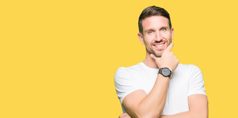 Handsome man wearing casual white t-shirt looking confident at the camera with smile with crossed arms and hand raised on chin. Thinking positive.