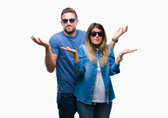Young couple in love wearing sunglasses over isolated background clueless and confused expression...