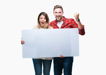Young couple together holding blank banner over isolated background screaming proud and celebrating...