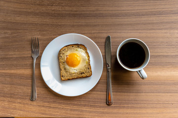 Breakfast concept. White plate with baked bread and egg and white coffee cup. Wooden texture background.