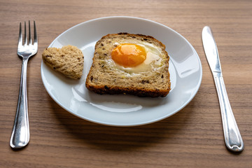 Breakfast concept. White plate with hearts of bread, baked bread and egg. Wooden texture background.