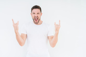 Young handsome man wearing casual white t-shirt over isolated background shouting with crazy expression doing rock symbol with hands up. Music star. Heavy concept.