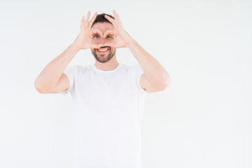 Young handsome man wearing casual white t-shirt over isolated background Doing heart shape with hand and fingers smiling looking through sign