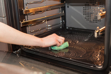 Housework and housekeeping concept. Scrubbing the stove and oven. Female hand with green sponge...