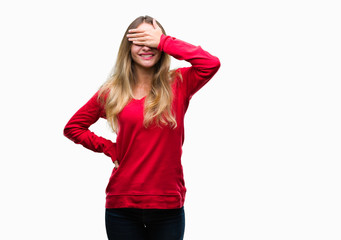 Obraz na płótnie Canvas Young beautiful blonde woman wearing red sweater over isolated background smiling and laughing with hand on face covering eyes for surprise. Blind concept.
