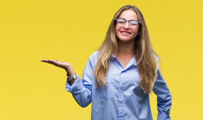 Young beautiful blonde business woman wearing glasses over isolated background smiling cheerful presenting and pointing with palm of hand looking at the camera.