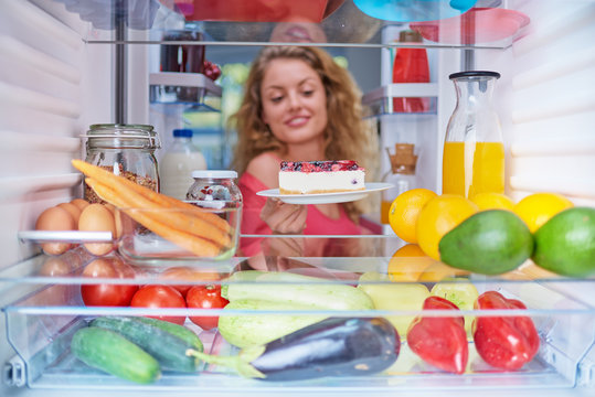  Woman taking gateau form fridge full of groceries. Unhealthy eating concept. Picture taken from the inside of fridge.