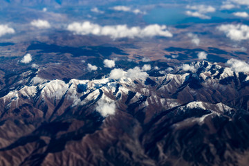Fototapeta premium Aerial view of large snow capped mountains surrounded by dry desert