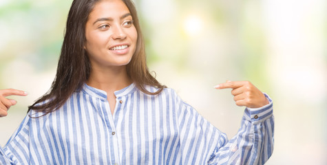 Young beautiful arab woman over isolated background looking confident with smile on face, pointing...