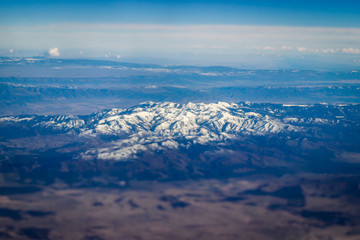 Fototapeta na wymiar Aerial view of large snow capped mountains surrounded by dry desert