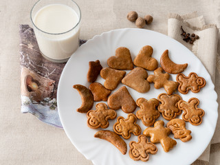 The glass of the milk with handmade's cakes on the plate near serviettes with  allspices and other spices on the natural tablecloth