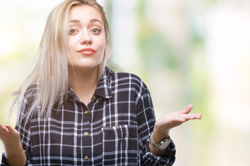 Young blonde woman over isolated background clueless and confused expression with arms and hands raised. Doubt concept.