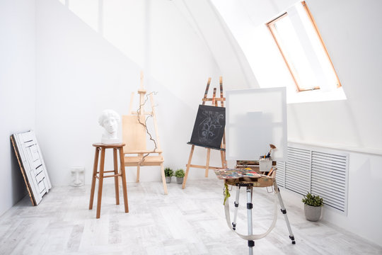 Interior of white studio of the artist, creative person. Easel, brushes, plaster head and figures. Attic, high ceilings.