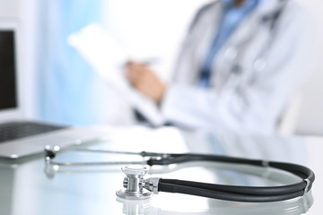 Stethoscope lying on glass desk with laptop computer at busy physician background. Medicine or pharmacy concept. Medical tools at doctor working table