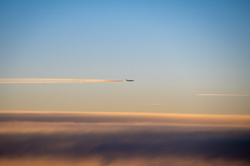 Fototapeta na wymiar Condensation trails behind airplane in high altitude glowing in sunset