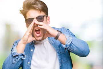 Young handsome man wearing sunglasses over isolated background Shouting angry out loud with hands over mouth