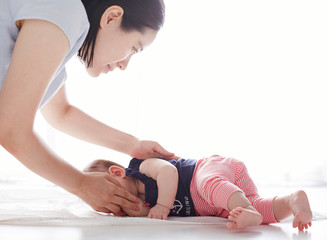 Naklejka premium Asian baby practicing turning over with the help of mother