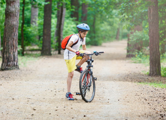 Child teenager in white t shirt and yellow shorts on  bicycle ride in  forest at spring or summer. Happy smiling Boy cycling outdoors. Active lifestyle, hobby