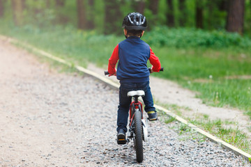 Child boy in blue t shirt on  bicycle ride in  forest at spring or summer. Happy little boy in helmet cycling outdoors. Active lifestyle, hobby
