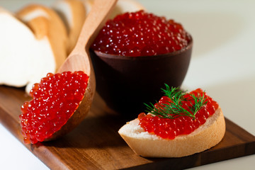 red caviar in a ceramic dish on a wooden platform on a white background
