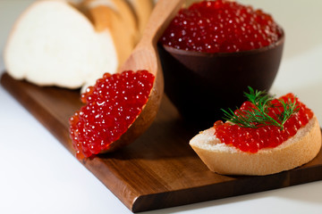 red caviar in a ceramic dish on a wooden platform on a white background