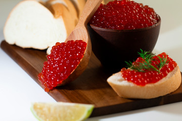 red caviar in a ceramic dish on a wooden platform on a white background